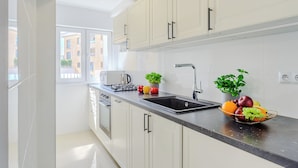 A modern kitchen with white cabinets, a black countertop, a sink, a stove, and a window providing a view of buildings outside.
