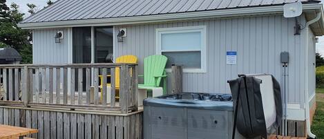 A small, single-story cabin with a metal roof, a deck, and a hot tub.