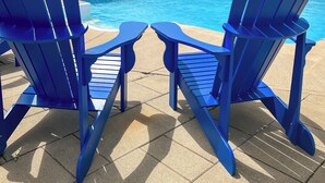 Dos sillas Adirondack azules mirando a una piscina con una valla de madera al fondo.