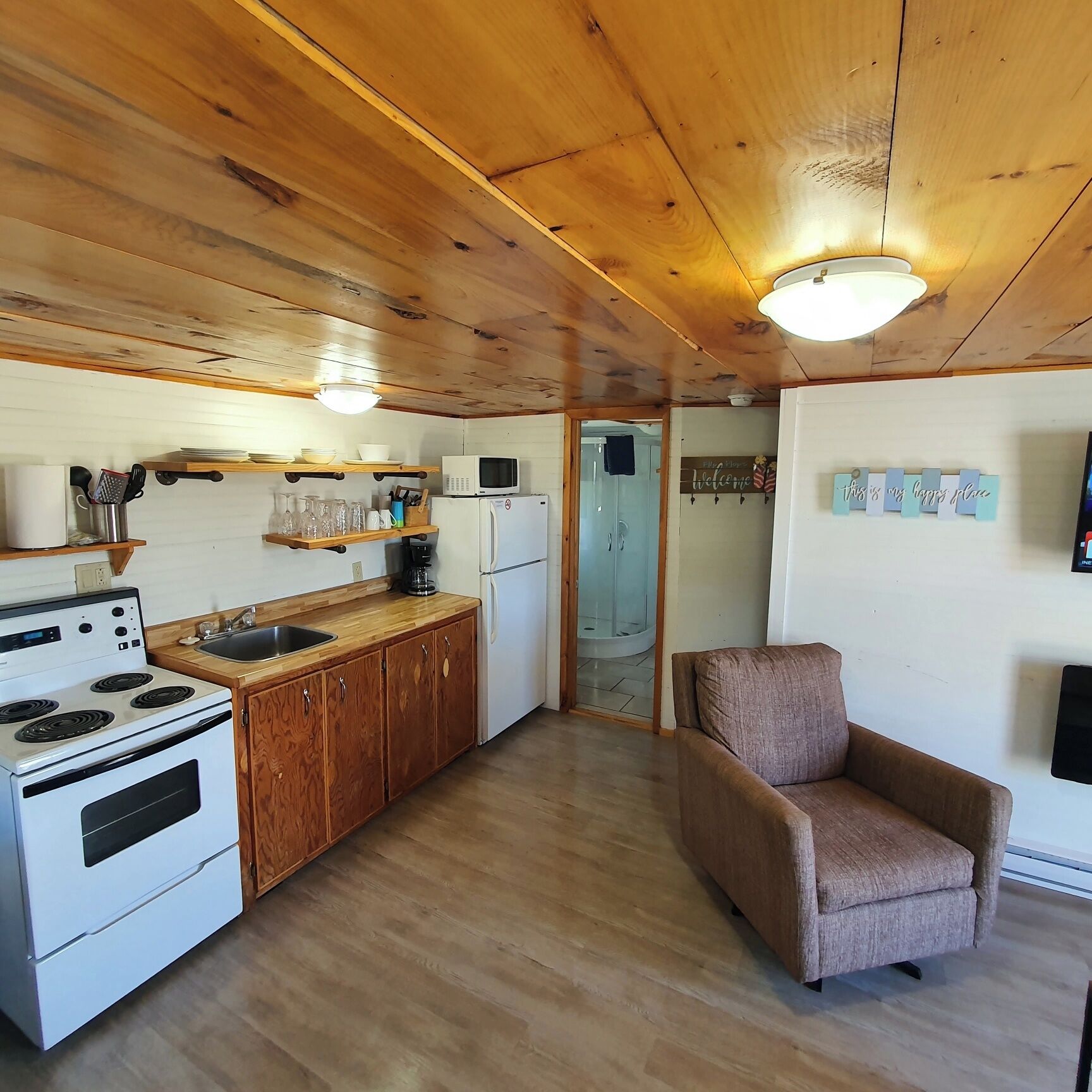A compact kitchen with wooden cabinets, a white stove, and a microwave. There's a small seating area with a brown chair.