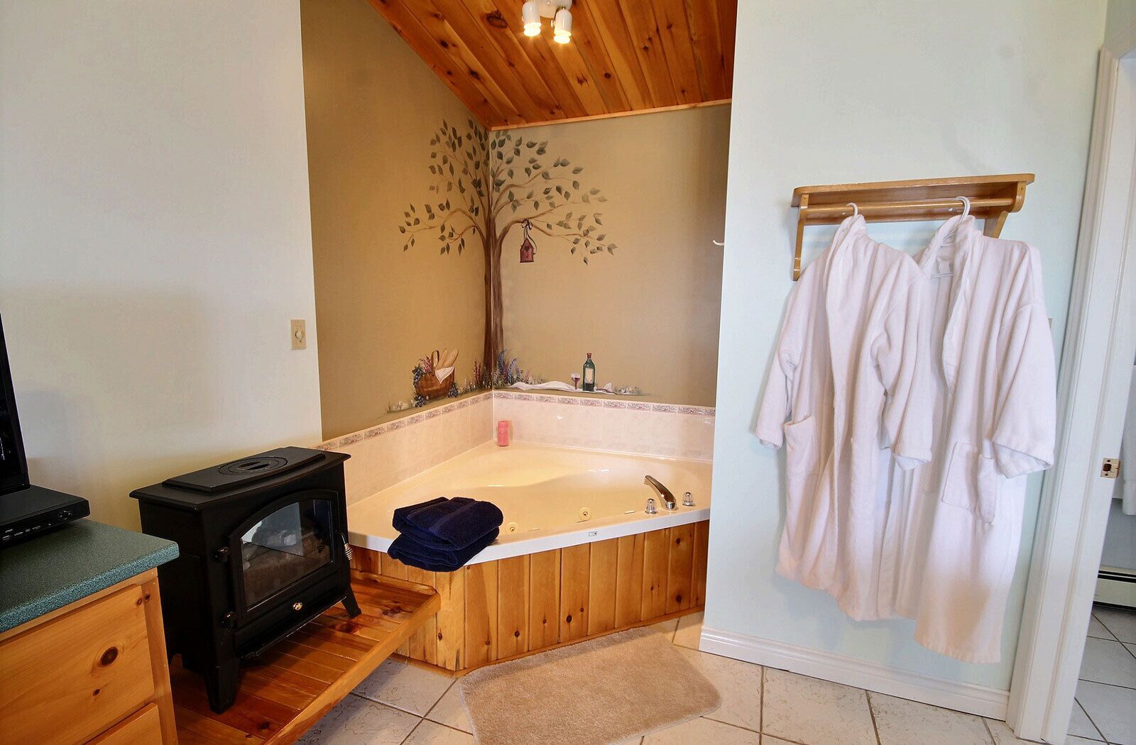 A bathroom with a wooden bathtub, a wooden heater, and a towel rack with robes.