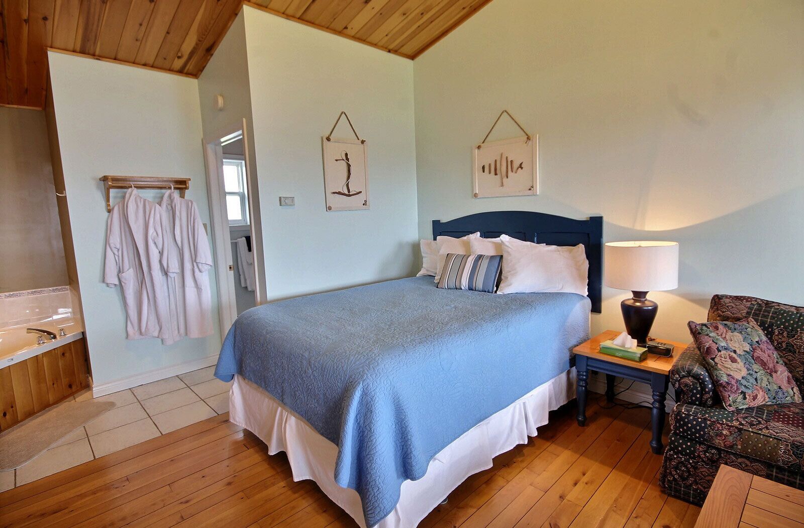 A bedroom with a bed, a nightstand, a lamp, a chair, and a wooden floor.