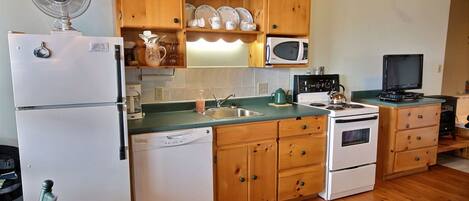 A compact kitchen with wooden cabinets, a microwave, a stove, and a dishwasher.