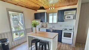 Una cocina moderna con techo de madera, armarios blancos, una isla central con taburetes y un amplio ventanal que proporciona luz natural.