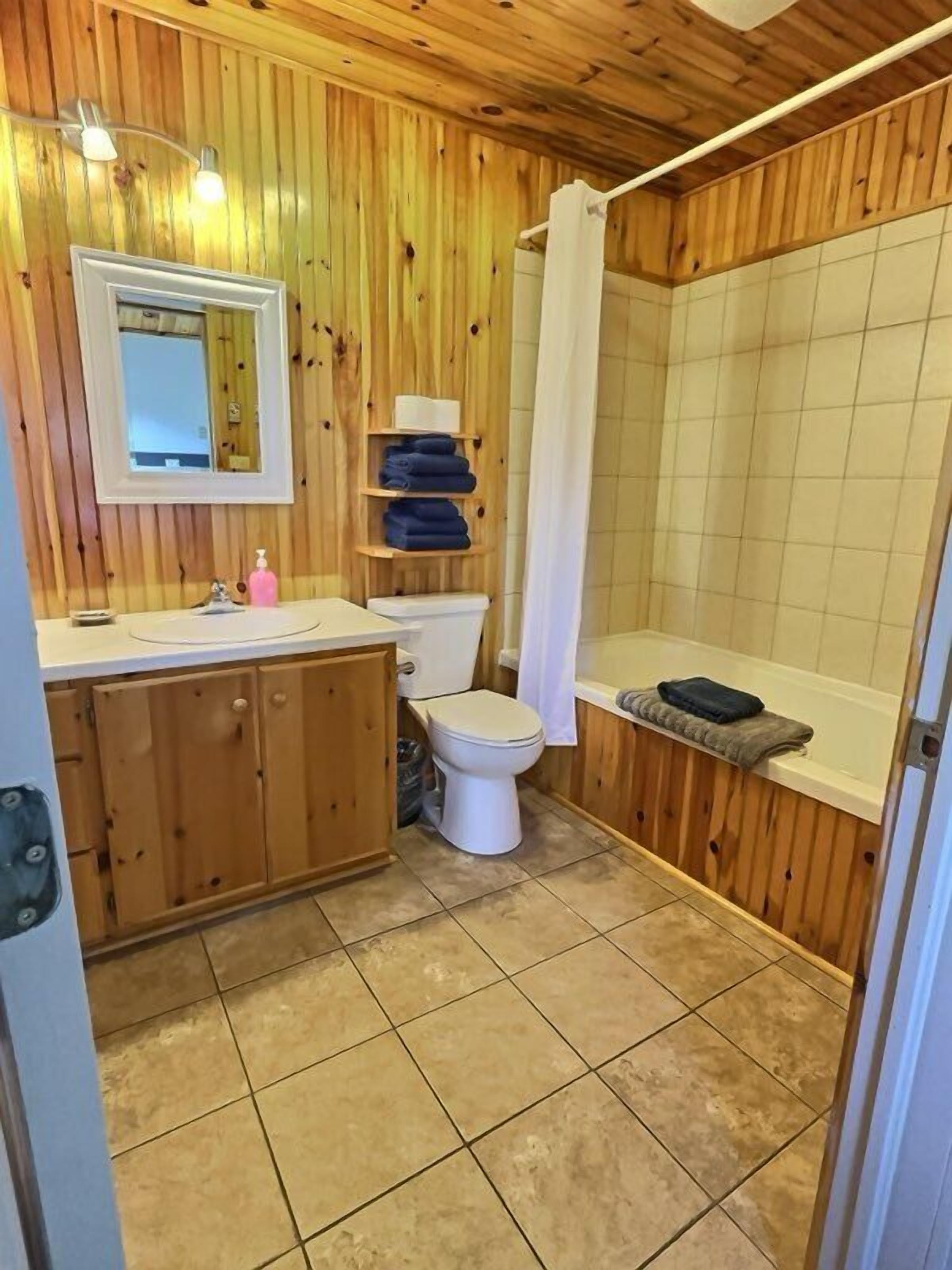 Une salle de bain aux murs lambrissés, équipée de toilettes, d’un lavabo et d’une douche.