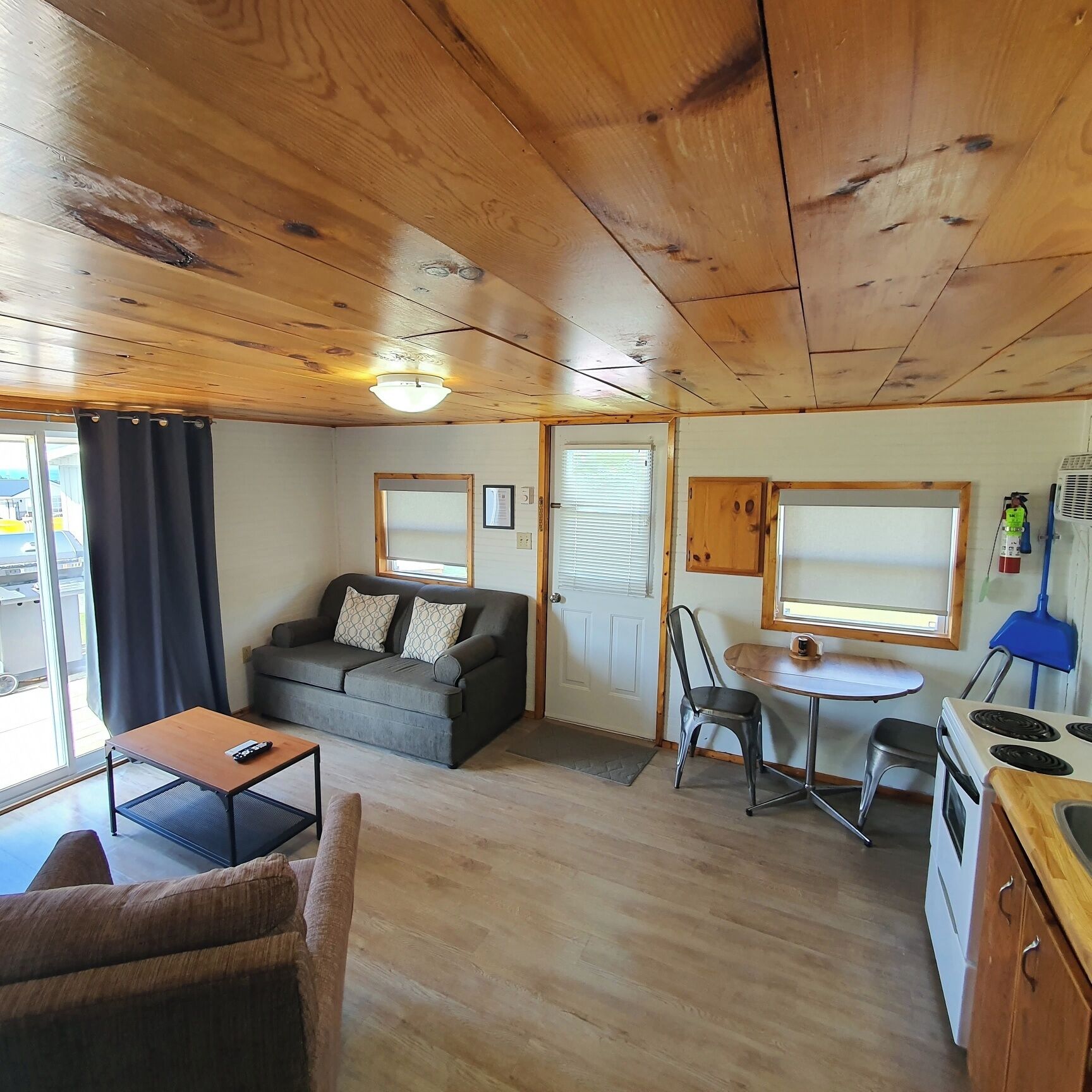 L’intérieur chaleureux d’un chalet avec un plafond en bois, un canapé, une table à manger avec des chaises, un coin cuisine et une fenêtre avec des rideaux.