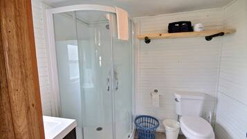 Une salle de bain avec une douche à parois de verre, des toilettes, un lavabo et une étagère contenant des articles de toilette.