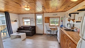 Interior acogedor de una cabaña con techo de madera, sala de estar con sofá y mesa de centro, cocina con pileta y estufa, y un cartel que dice 'Allan's Cottage'.