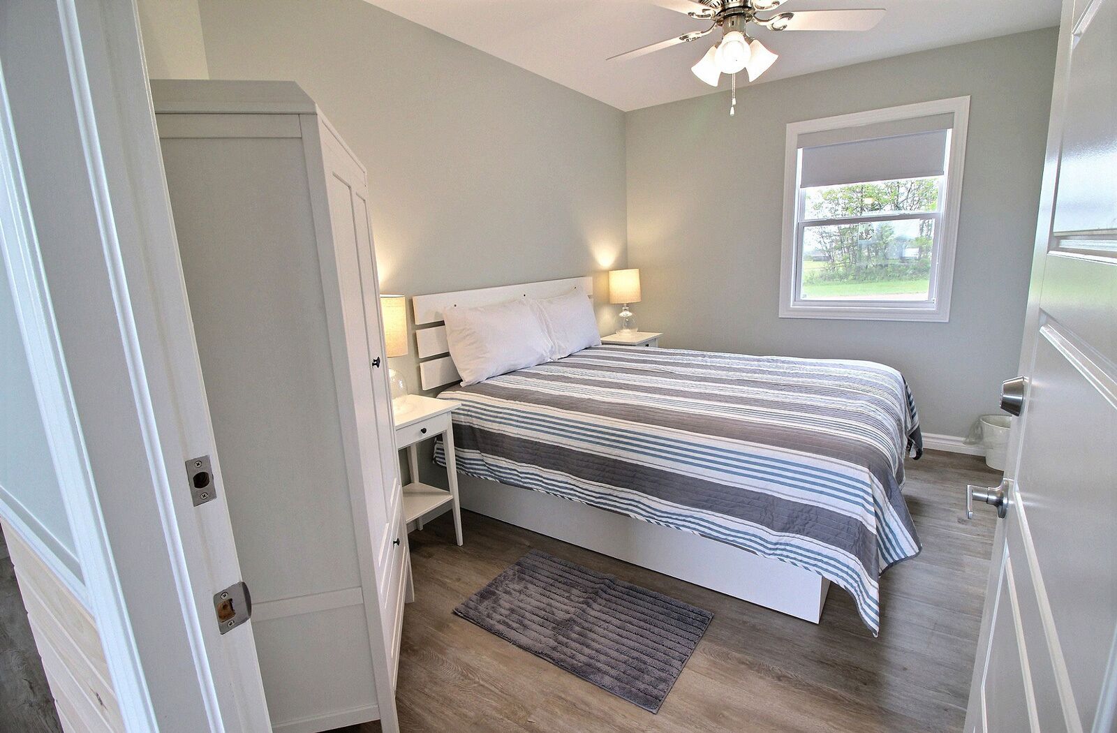 A bedroom with a bed, bedside tables, a ceiling fan, a window, and a door.