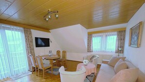 A cozy living room with a wooden floor, a round table with chairs, a sofa, and a television mounted on the wall. - Apartment, 55sqm with 8sqm balcony, 2-4persons in Baiersbronn center (Baiersbronn)