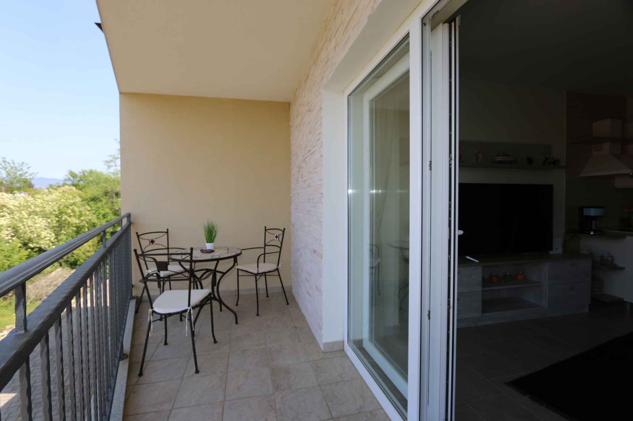 Ein Balkon mit Tisch und Stühlen, eine Glasschiebetür, die zu einem Wohnbereich mit Fernseher und Küchengeräten führt.