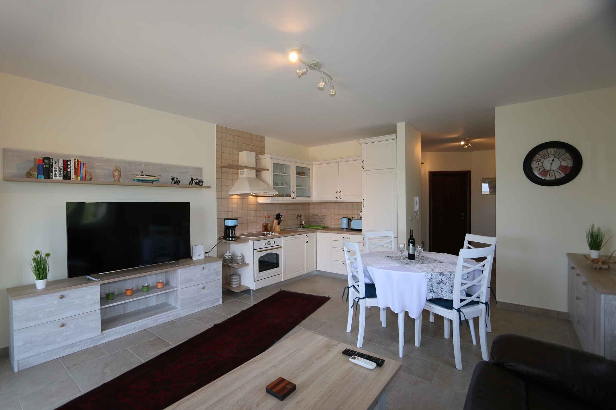 A modern kitchen with white cabinets, a built-in oven, and a dining area with a table and chairs.