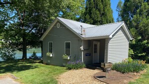 En liten, envåningsstuga med ett tak av metall, en veranda och en skylt med texten ”Maddalena Point Cottage”.