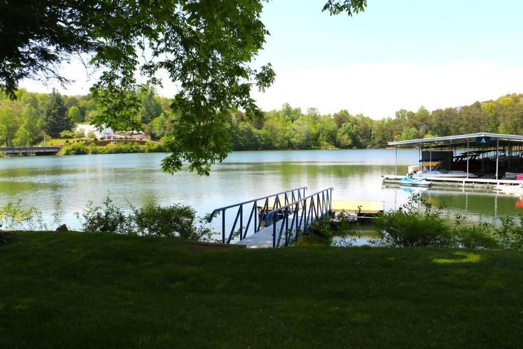 A lakeside dock with a covered boat ramp, a grassy area, and a house in the background.