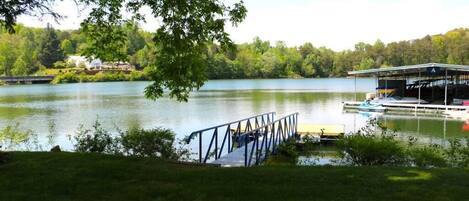 A lakeside dock with a covered boat ramp, a grassy area, and a house in the background.