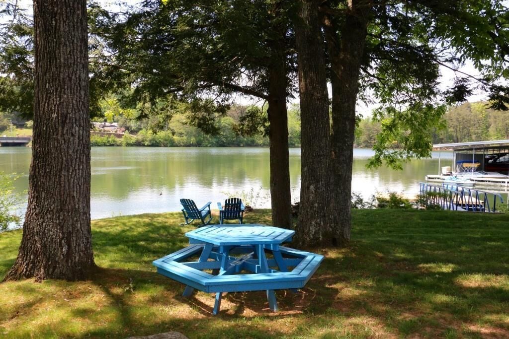 Ein Picknicktisch mit zwei Stühlen am Seeufer, umgeben von Bäumen.