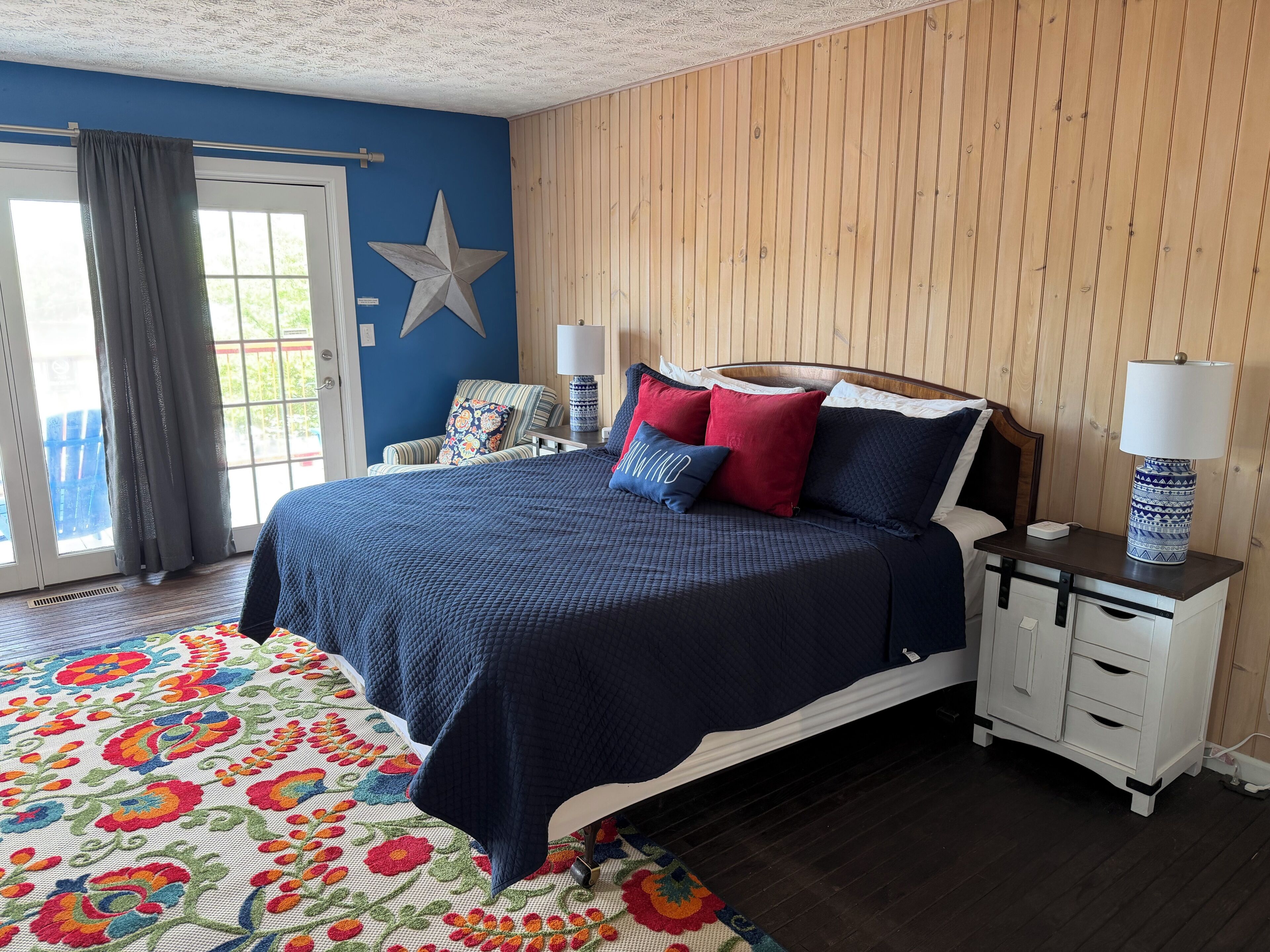 A bedroom with a bed, nightstands, a star decoration, a window with curtains, and a floral-patterned rug.