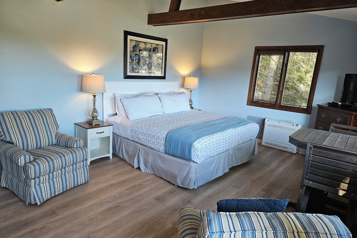 A bedroom with a bed, two bedside tables with lamps, a window, and a wooden ceiling.