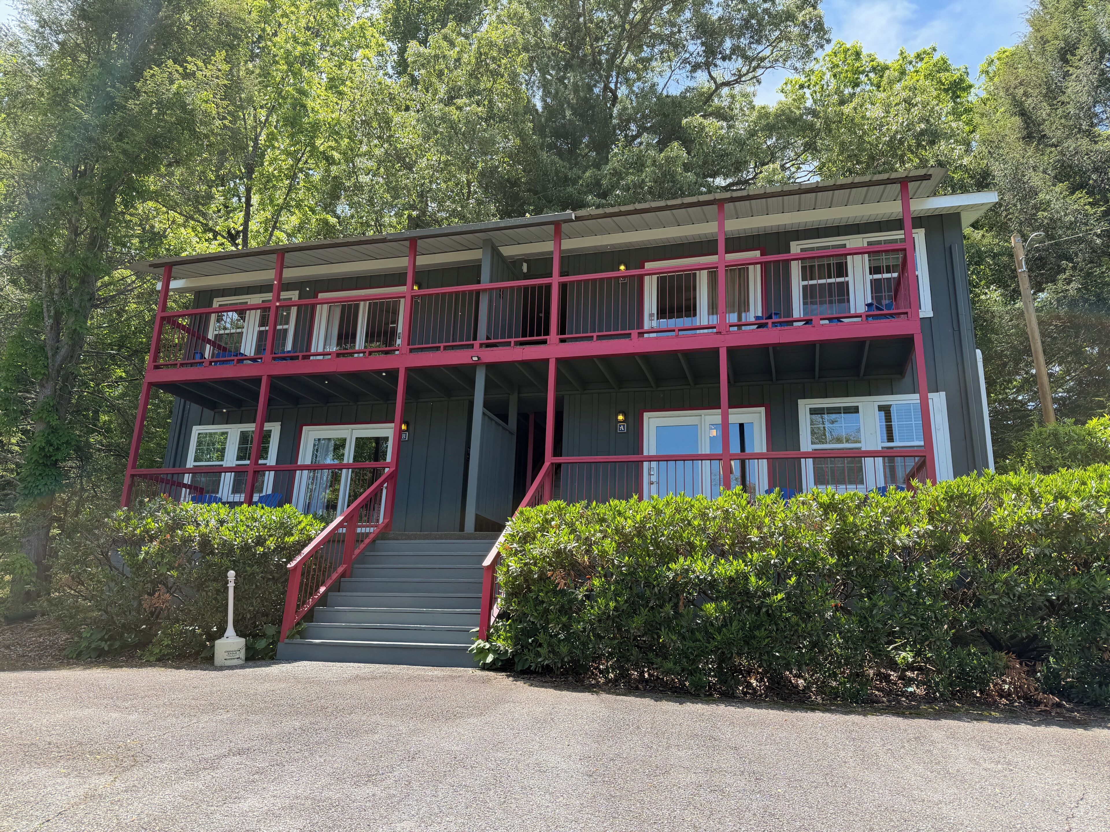 A two-story building with a red exterior, a staircase leading to the entrance, and a surrounding lush green landscape.