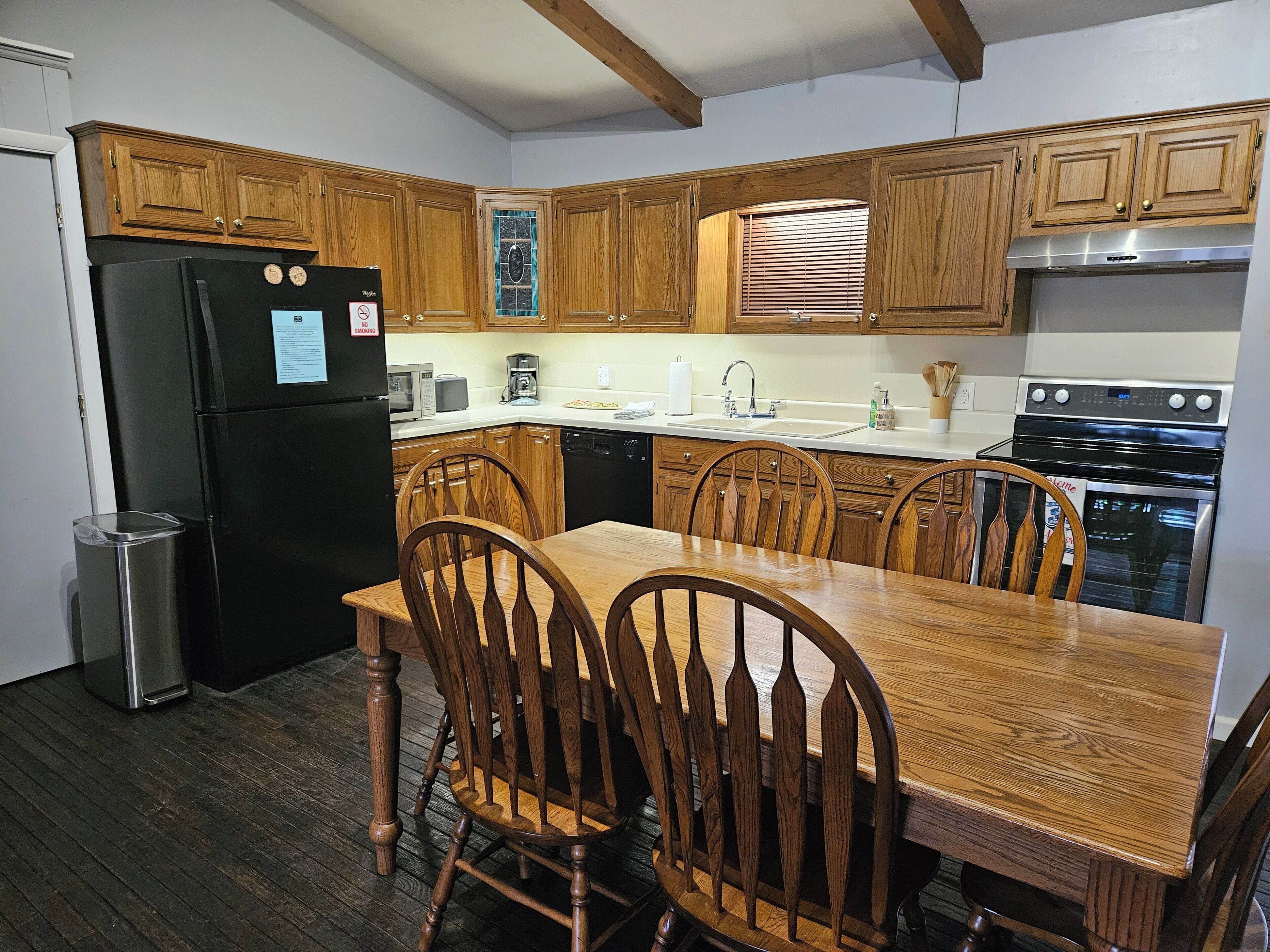 Una cocina con armarios de madera, un refrigerador negro, una estufa y una mesa de comedor con sillas.