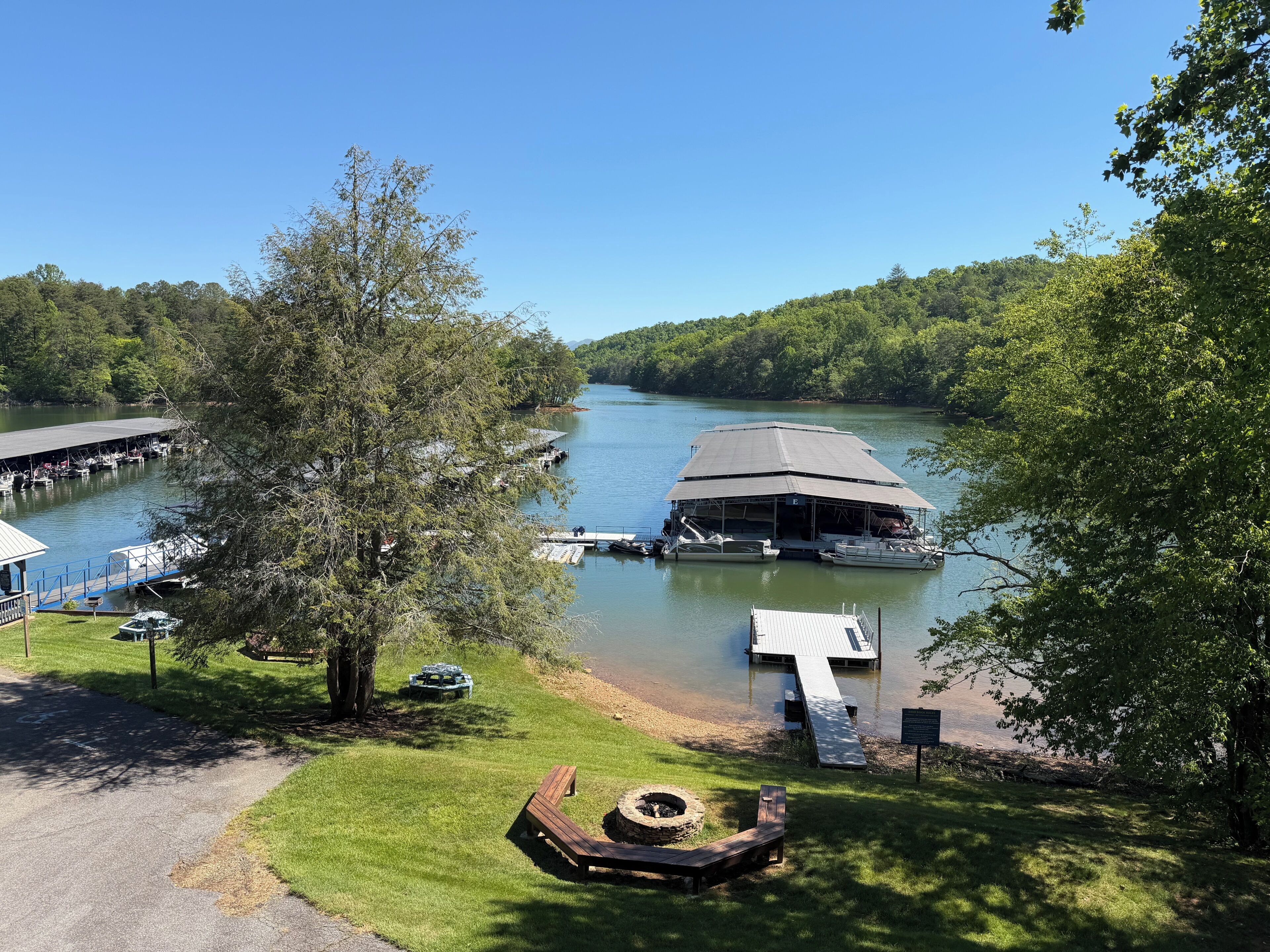 A lakeside dock with a covered boat ramp, a boat house, and a fire pit area.