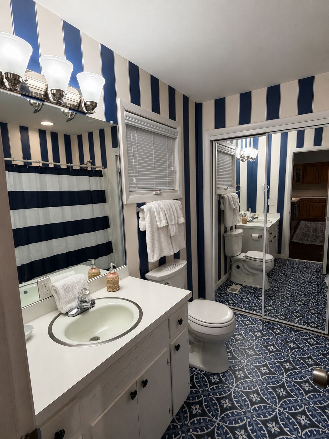Ein Badezimmer mit gestreifter Wandgestaltung, einem Waschbecken, zwei Toiletten und einem Spiegel.