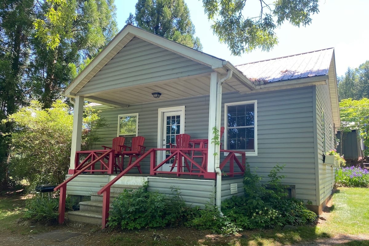 A small, single-story house with a porch, red railings, and a front door.