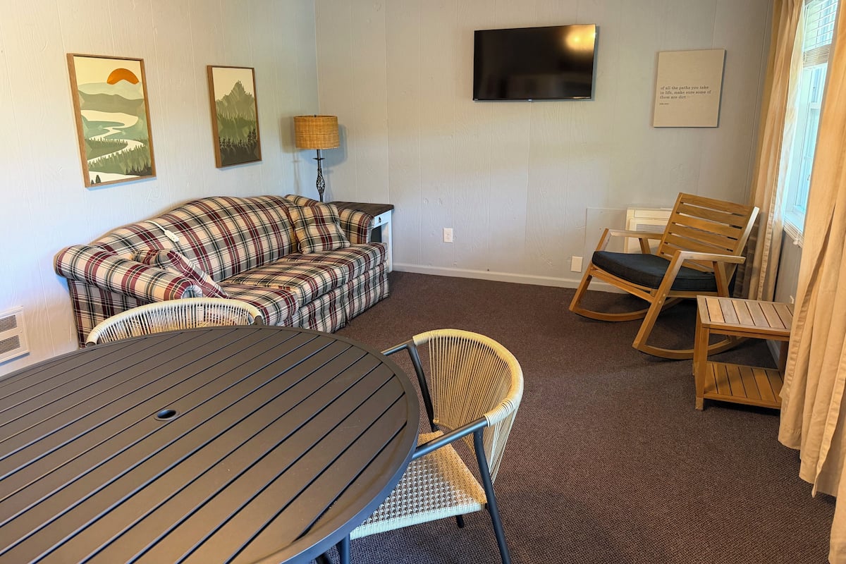 A room with a plaid sofa, a dining table, a TV, and a chair.