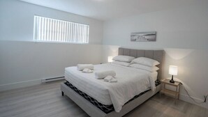 A modern bedroom with a bed, bedside lamps, a window with blinds, and a painting on the wall. - Stylish, Modern 3BR in Moncton (Moncton)