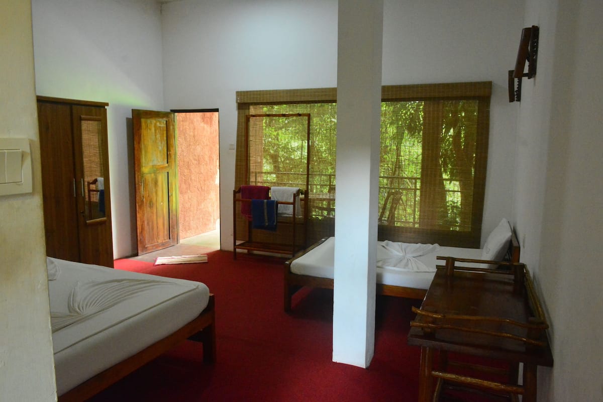 Una habitación con dos camas, una mesa de madera y una ventana con vistas a árboles.