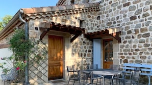 Un bâtiment en pierre avec une porte en bois et un patio couvert comprenant des chaises et une table en métal.