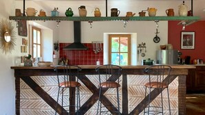Une cuisine dotée d’un îlot central, de tabourets de bar, de casseroles suspendues et d’un dosseret de crédence en carreaux rouges.