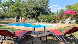 Un jardin avec une piscine, des chaises longues et un parasol rouge.