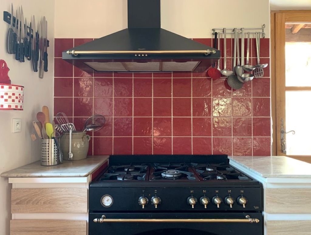 A kitchen with a gas stove, a black range hood, and red tiled backsplash.