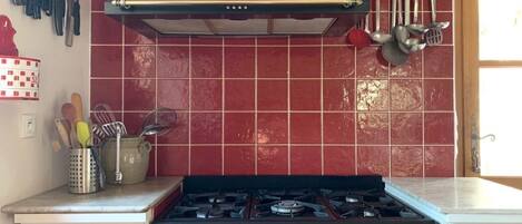 A kitchen with a gas stove, a black range hood, and red tiled backsplash.