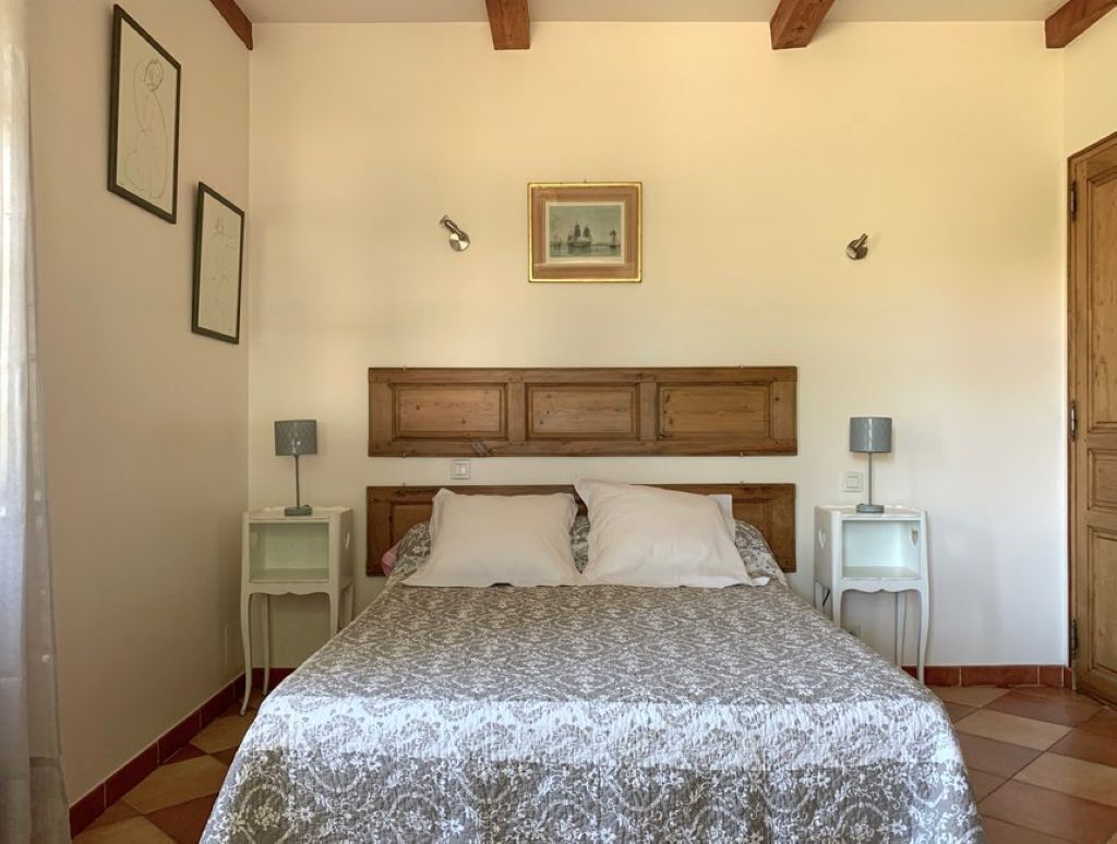 A bedroom with a patterned bedspread, wooden headboard, two bedside tables with lamps, and framed pictures on the wall.
