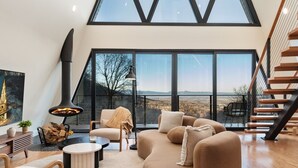 A modern living room with a large window, a fireplace, and a staircase. - Ava A-Frame•Hot Tub•Theater•Hidden Stair•EV Charge (Stanley)