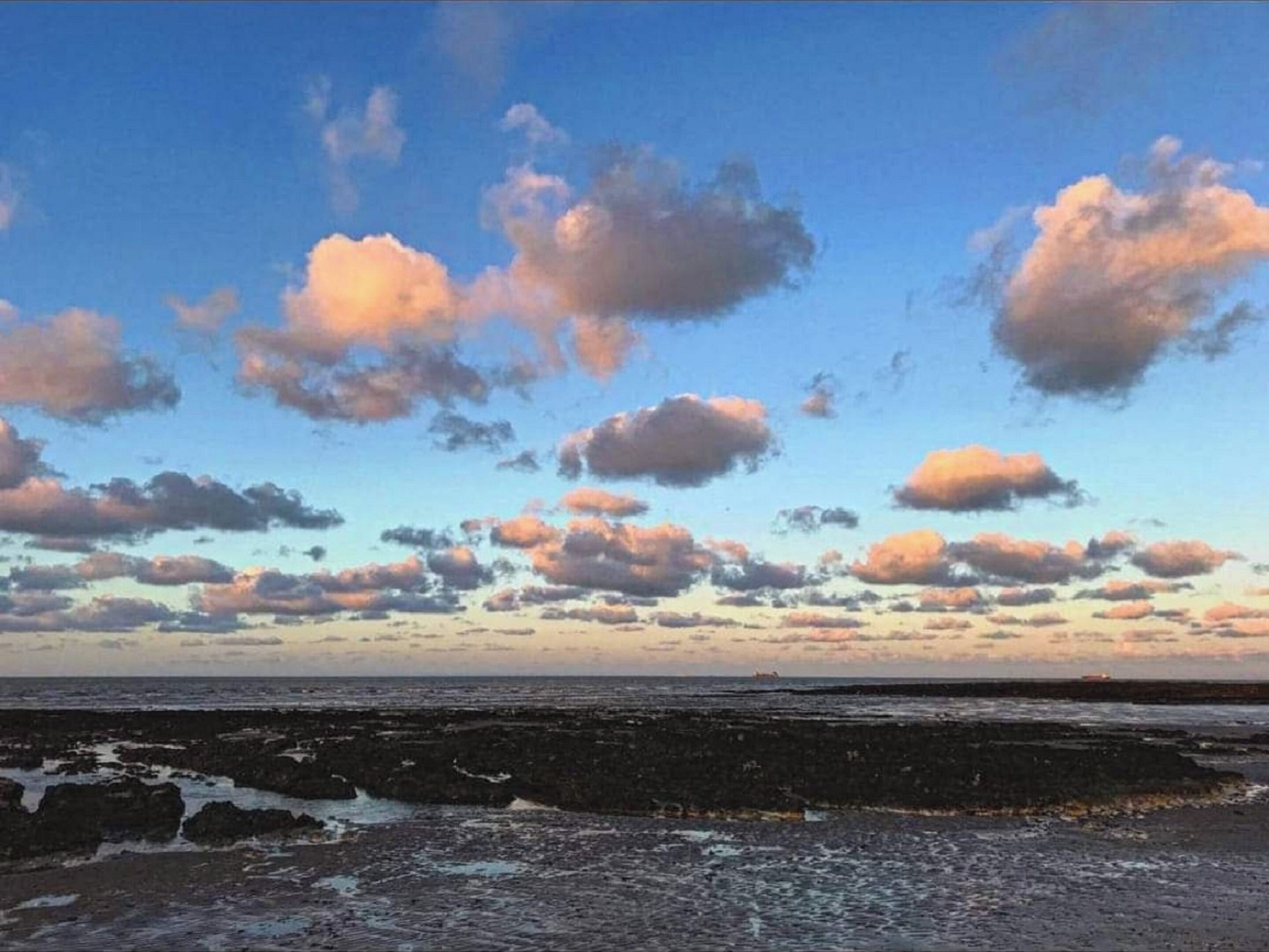 A coastal landscape with a rocky shoreline and a clear sky with scattered clouds.