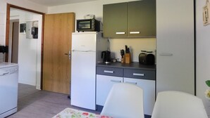 A compact kitchen with a microwave, toaster, and a refrigerator. There is a wooden door leading to another room, and a white chair is visible. - 1 Bedroom Apartment in Zierow (Zierow)