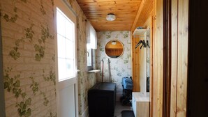A narrow hallway with a wooden ceiling, a brick wall with ivy, a round mirror, and a bench. - 1 Bedroom Apartment in Zierow (Zierow)