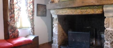 Una sala de estar acogedora con chimenea de piedra, un sofá rojo y una ventana con cortinas florales.