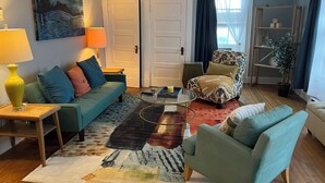 A living room with a sofa, armchair, coffee table, and a painting on the wall.