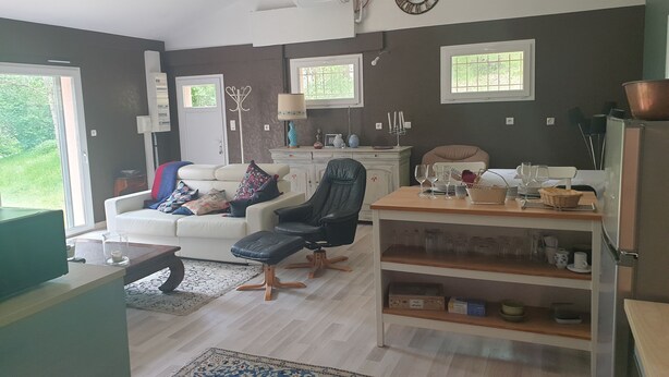Een ruime woonkamer met een witte bank, een zwarte fauteuil en een eethoek met een houten tafel.