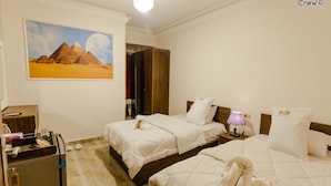 A hotel room with two beds, a desk, a wardrobe, and a painting of pyramids. - Pyramids Golden Gate Hotel (Giza)