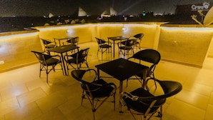An outdoor seating area with tables and chairs, a tiled floor, and a low wall. - Pyramids Golden Gate Hotel (Giza)