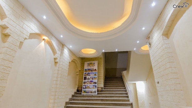 A staircase with a banner displaying photos, surrounded by white brick walls and recessed lighting. - Pyramids Golden Gate Hotel (Giza)