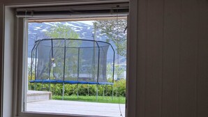Ein Fenster mit Blick auf ein Trampolin und grüne Bepflanzung.