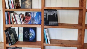 Ein Holzregal mit mehreren Ablagen, auf denen Bücher und ein kleiner Blumentopf stehen.