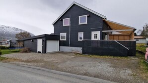 Ein zweigeschossiges Haus mit dunkler Fassade, einer kleinen Garage und einer Holzterrasse.