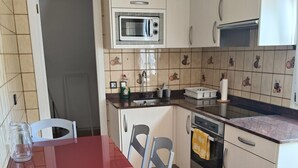 Una cocina compacta con microondas, horno y lavabo. Hay una mesa de comedor con sillas.